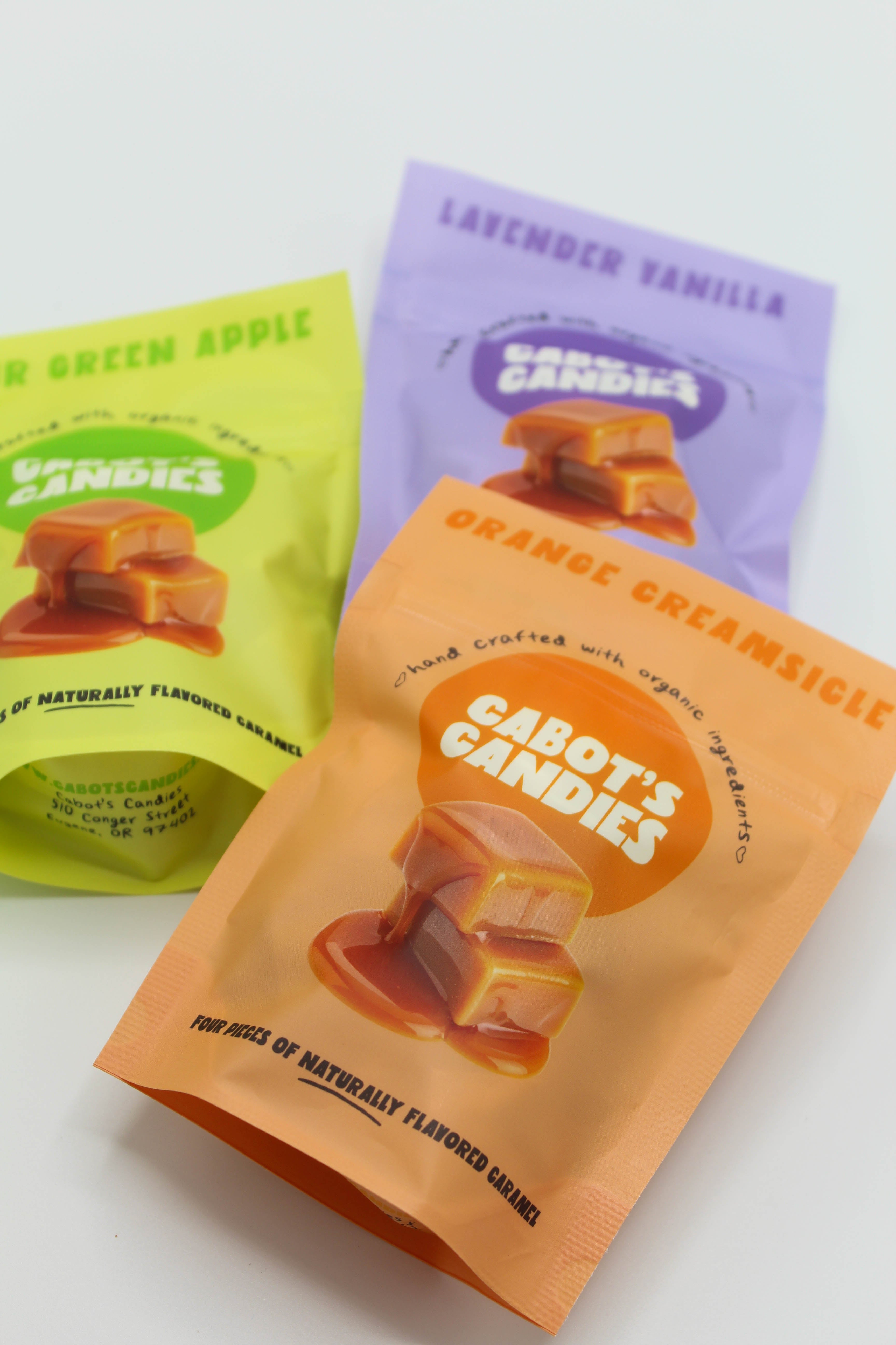 Three stand-up pouches of Cabot's Candies on a white background, including Green Apple, Orange Creamsicle, and Lavender Vanilla flavors.