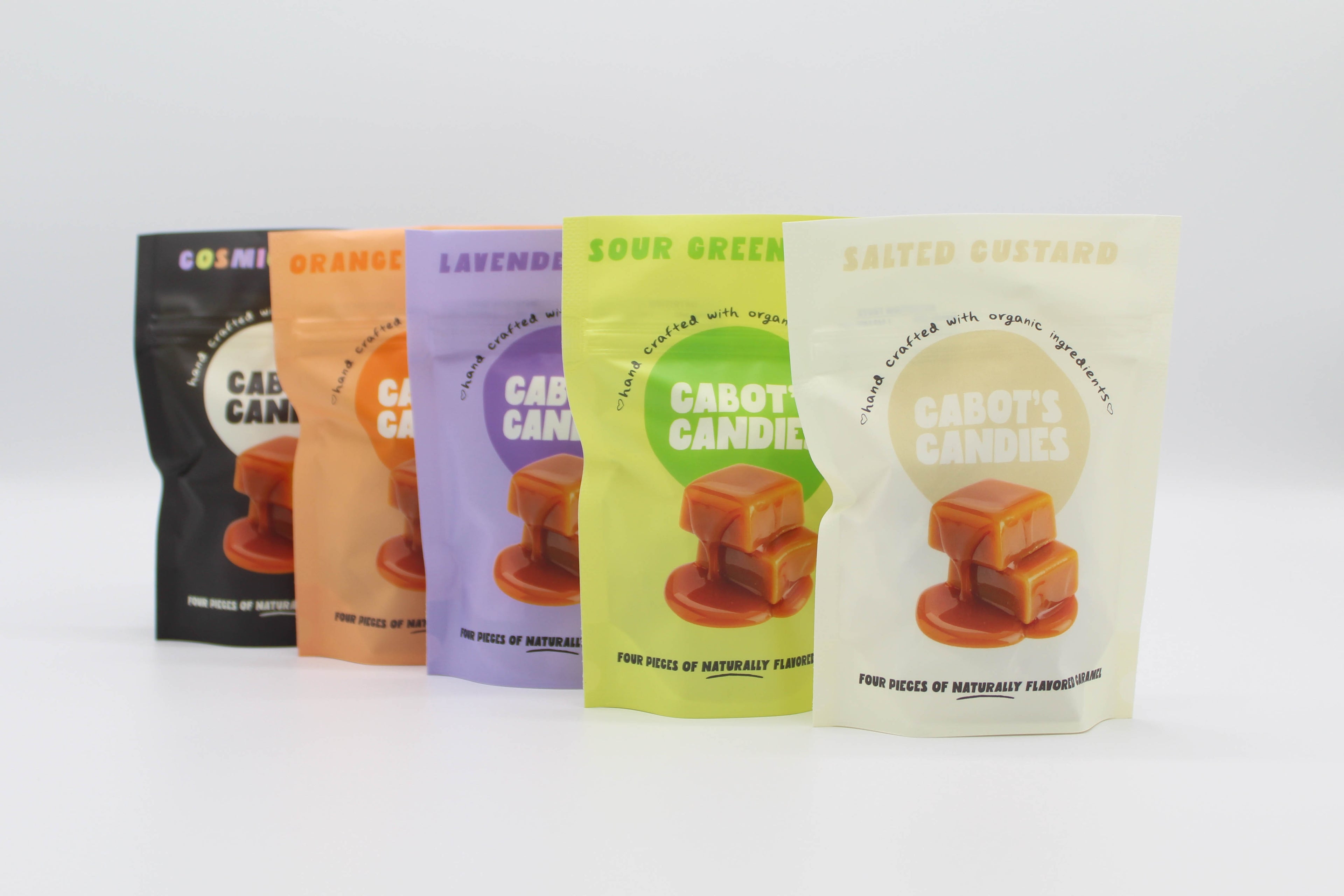 Four stand-up pouches of Cabot's Candies in different flavors (Cosmic, Orange, Lavender, Sour Green, and Salted Custard) lined up on a white background.